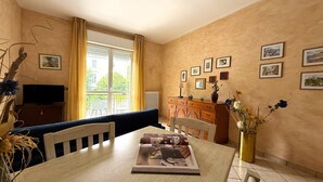 A dining area with a table, chairs, a sofa, a television, and a window with curtains. - Kennedy 2 - One Bedroom Apartment, Sleeps 3 (Albenga)