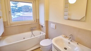 Un baño con bañera, inodoro y lavamanos. Hay una ventana sobre la bañera.