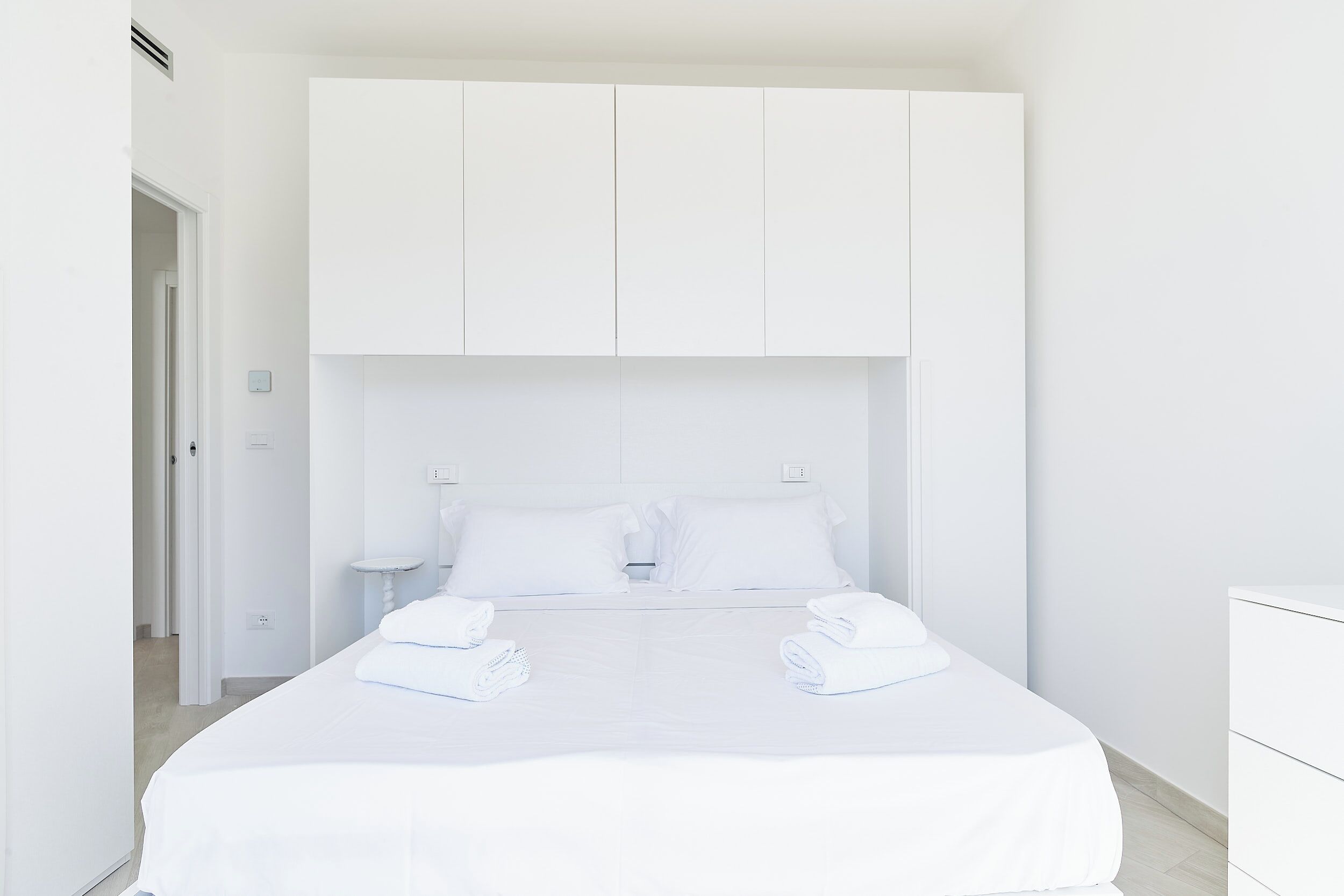 Una habitación de hotel con una cama grande, cabecera blanca y una mesita de noche.