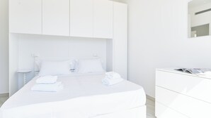 A modern hotel room with a large bed, white bedding, a bedside table, and a dresser. - The Italian Lady - Unit 1 (Alassio)