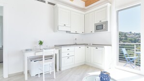 A modern kitchen with white cabinetry, a microwave, and a dining area with a white table and chairs. - The Italian Lady - Unit 1 (Alassio)