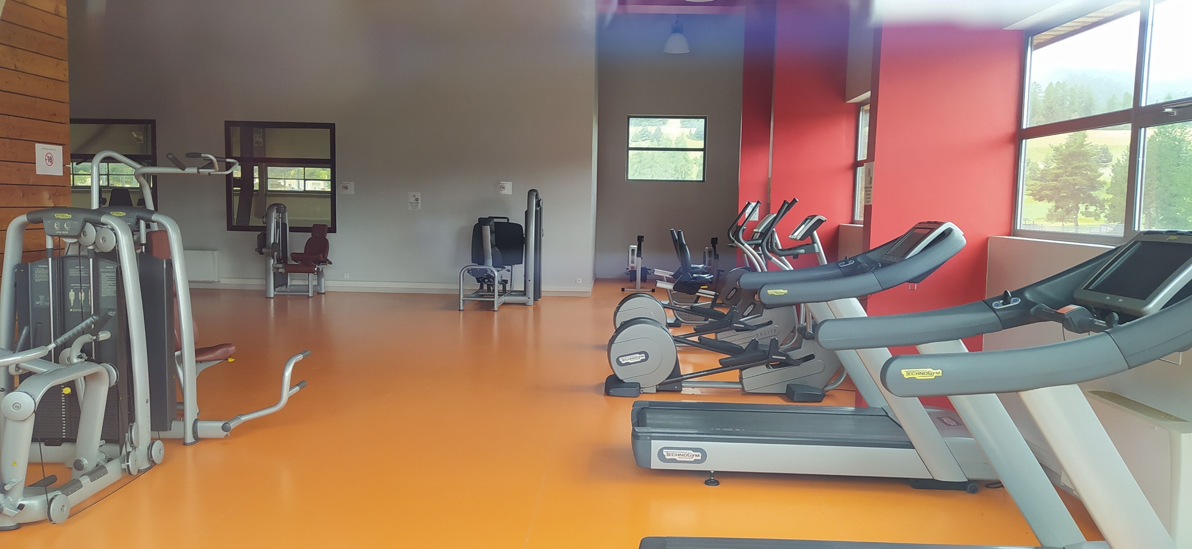 A gym with cardio equipment, weight machines, and a red wall.