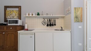 A compact kitchen with a microwave, a refrigerator, and a shelf with kitchen utensils. - Italianway Comfort - Rosmini 13 D (Milano)