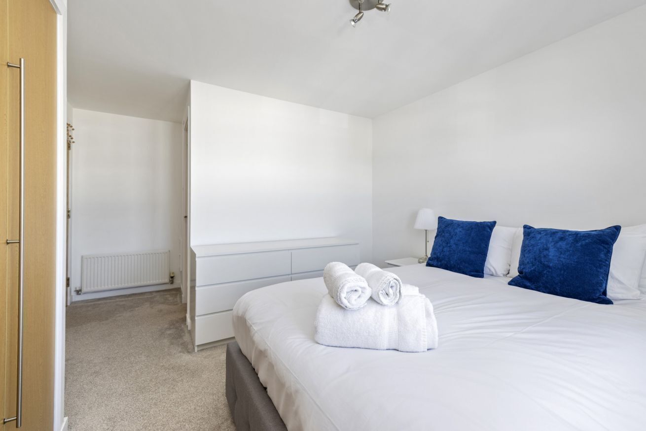 A hotel room with a large bed, a bedside table, a lamp, and a wardrobe.
