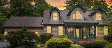 A two-story house with a front porch, a flag, and a well-maintained garden.