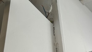 Ein Raumeck mit weißen Wänden und freiliegenden Kabeln.