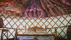 A bed with a wooden headboard, a diamond-patterned wall, and a tapestry with paisley designs. - Brandon House Farm Yurt (Norwich)