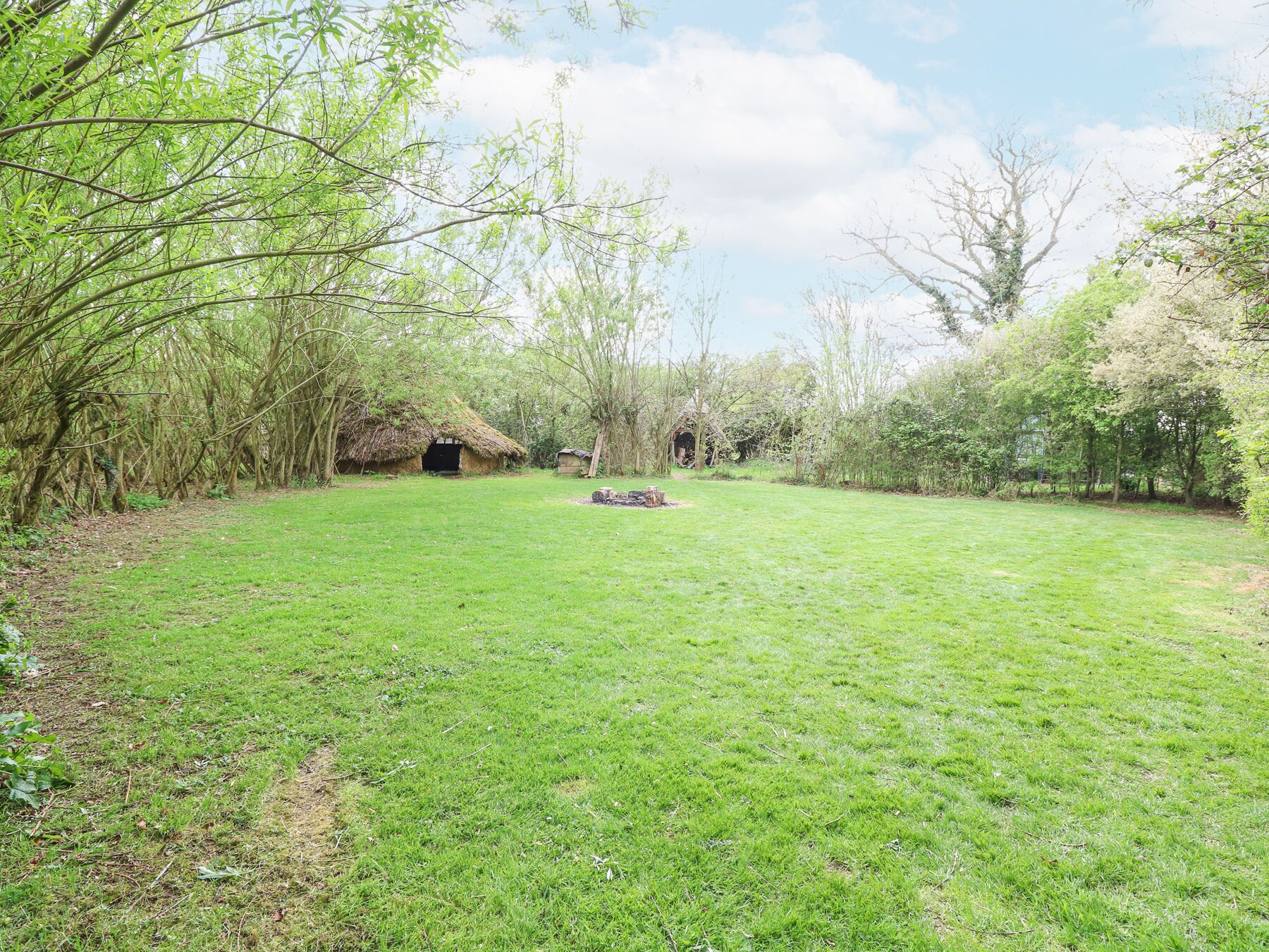 A grassy area with a thatched-roof structure and a stone wall in the background.