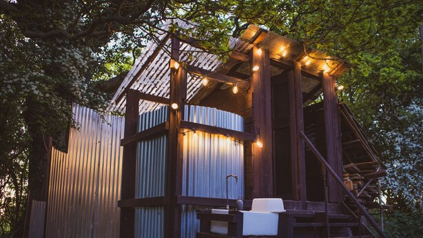 A rustic wooden structure with a metal exterior, a staircase, and string lights. - Brandon House Farm Yurt (Norwich)