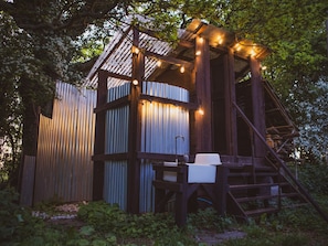A rustic wooden structure with a metal exterior, a staircase, and string lights. - Brandon House Farm Yurt (Norwich)