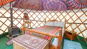 A traditional wooden bed with a colorful striped bedspread, a woven basket, and a small wooden nightstand. - Brandon House Farm Yurt (Norwich)