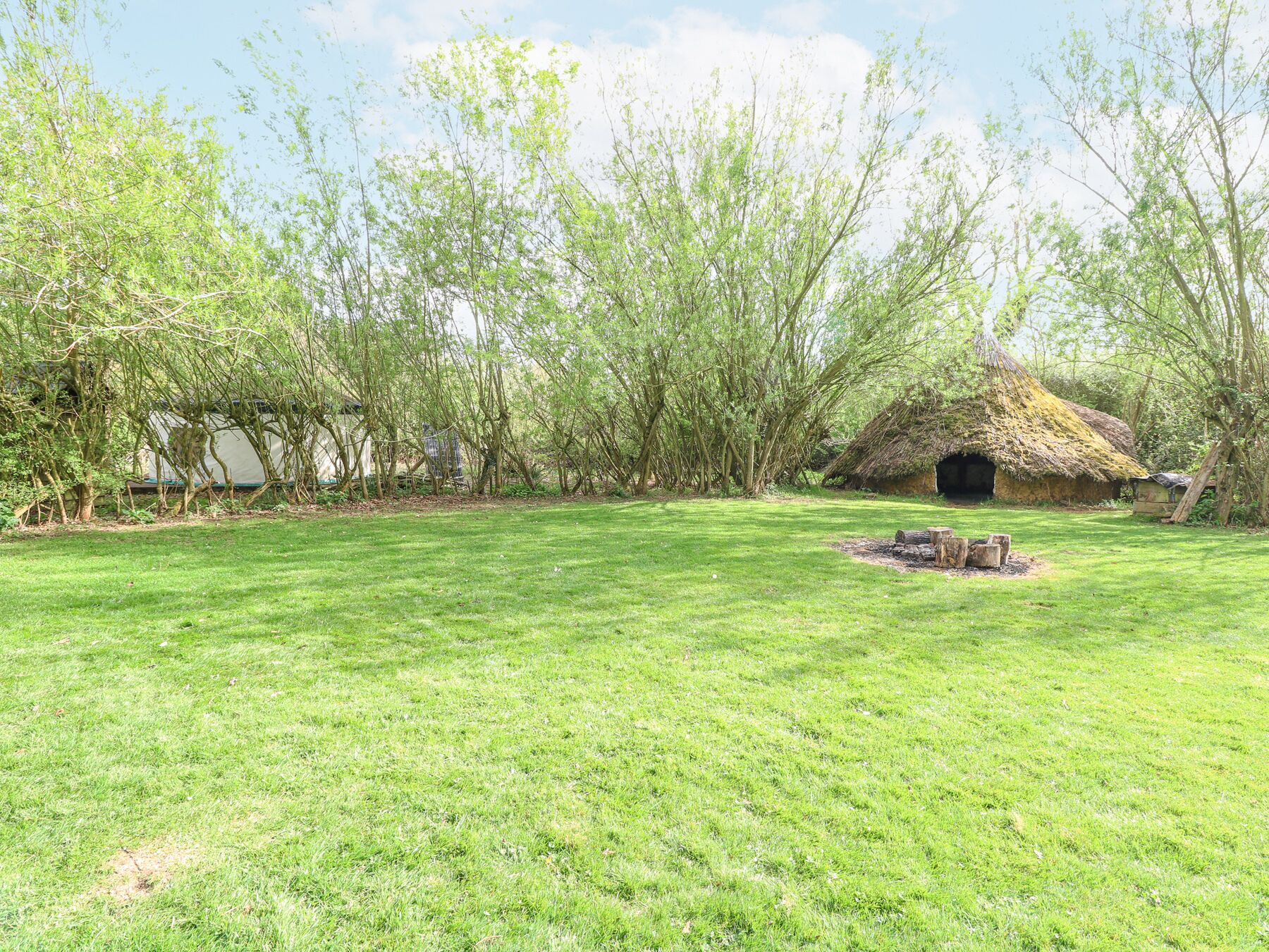 A grassy area with a thatched-roof hut and trees.
