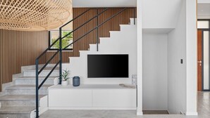 A modern staircase with a black metal railing, a flat-screen TV mounted on the wall, and a woven rattan light fixture above. - Ocean View Villa: Your Dream Getaway (Jesenice, Dugi Rat)