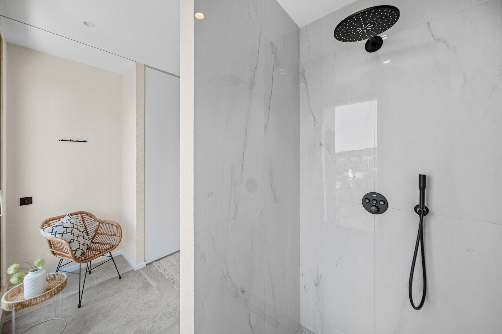 A modern bathroom with a shower, a chair, and a small table with a plant.