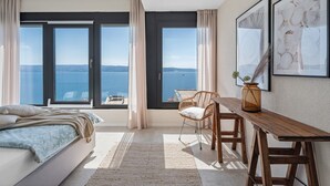 A bedroom with a bed, a desk, a chair, and large windows with a view of the sea. - Ocean View Villa: Your Dream Getaway (Jesenice, Dugi Rat)