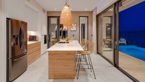 A modern kitchen with a central island, stainless steel appliances, and a dining area with wicker chairs. - Ocean View Villa: Your Dream Getaway (Jesenice, Dugi Rat)