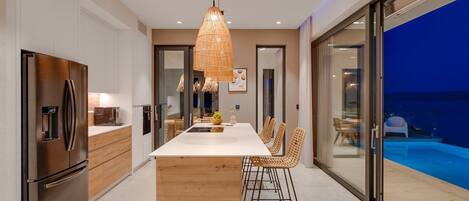 A modern kitchen with a central island, stainless steel appliances, and a dining area with wicker chairs.