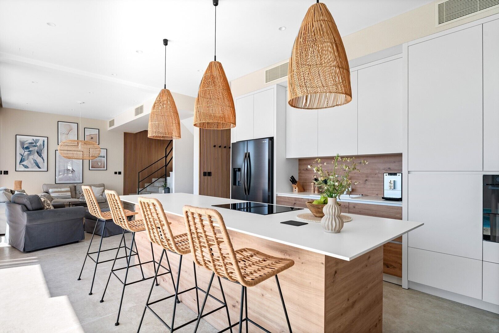 A modern kitchen with a central island, wicker pendant lights, and a dining area with wicker chairs.