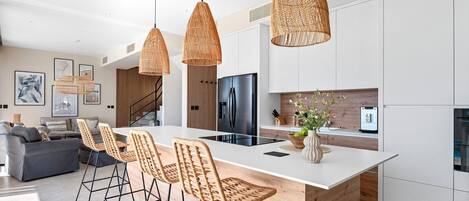 A modern kitchen with a central island, wicker pendant lights, and a dining area with wicker chairs.