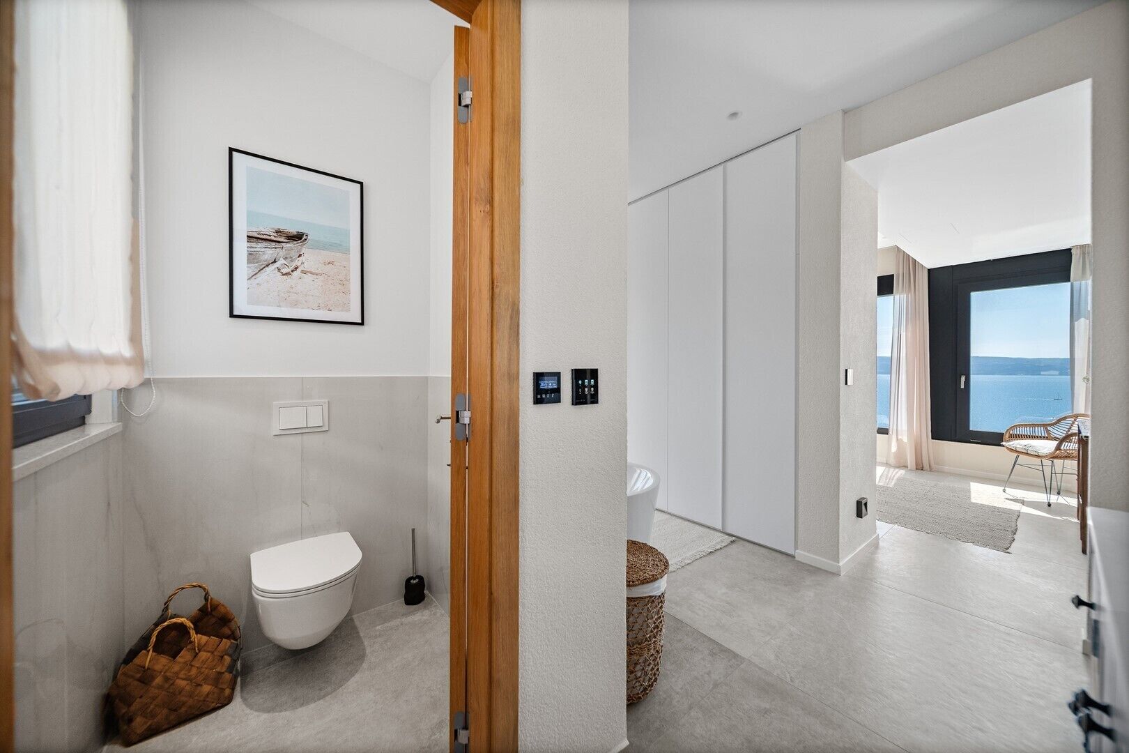 A modern bathroom with a toilet, a wooden door, and a framed picture on the wall.