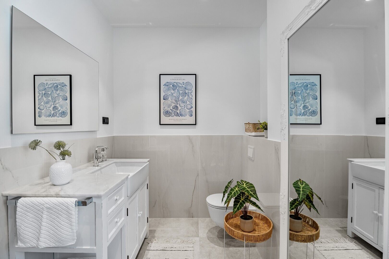 A modern bathroom with two sinks, a large mirror, and framed botanical prints on the wall.