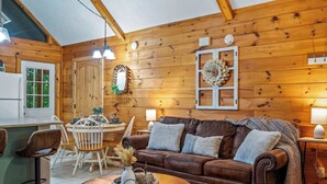 A cozy wooden cabin interior with a dining area, a brown leather sofa, and a coffee table.