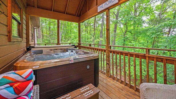 A wooden deck with a hot tub, a sign reading "The Porch," and a view of a forest.