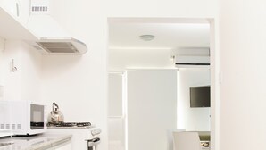 A modern kitchen with white cabinetry, a built-in microwave, and a stove. There is a dining area with a table and chairs. - Complejo 21 de Enero - Luz y Fuerza (Puerto Madryn)
