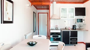 A modern kitchen with white cabinets, a stove, and a microwave. There is a dining table with chairs and a bowl of fruit. - Complejo 21 de Enero - Luz y Fuerza (Puerto Madryn)