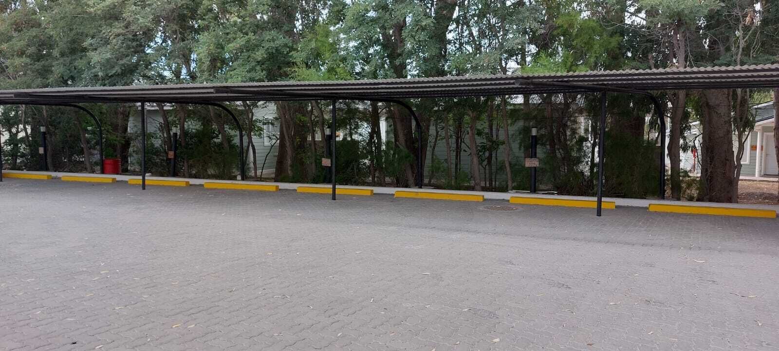 An outdoor covered parking area with yellow safety lines, surrounded by trees.