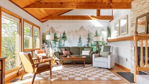 Ein gemütliches Wohnzimmer mit Holzbalkendecke, einem großen Fenster, einer Couch, einem Couchtisch und einem Kamin.
