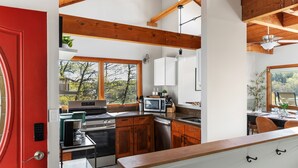 Eine moderne Küche mit Holzbalken, einem großen Fenster und einer roten Tür.