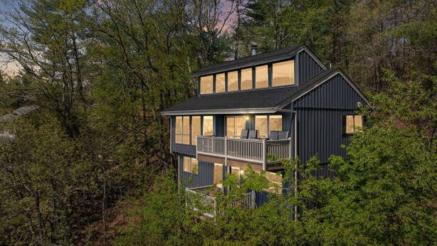 Ein modernes, zweistöckiges Haus mit Balkon, umgeben von dichtem Wald.