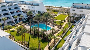 A resort with a pool surrounded by palm trees, a beach view, and multiple buildings with balconies. - Aegean 214 Gorgeous 2 bed/2 bath (Destin)