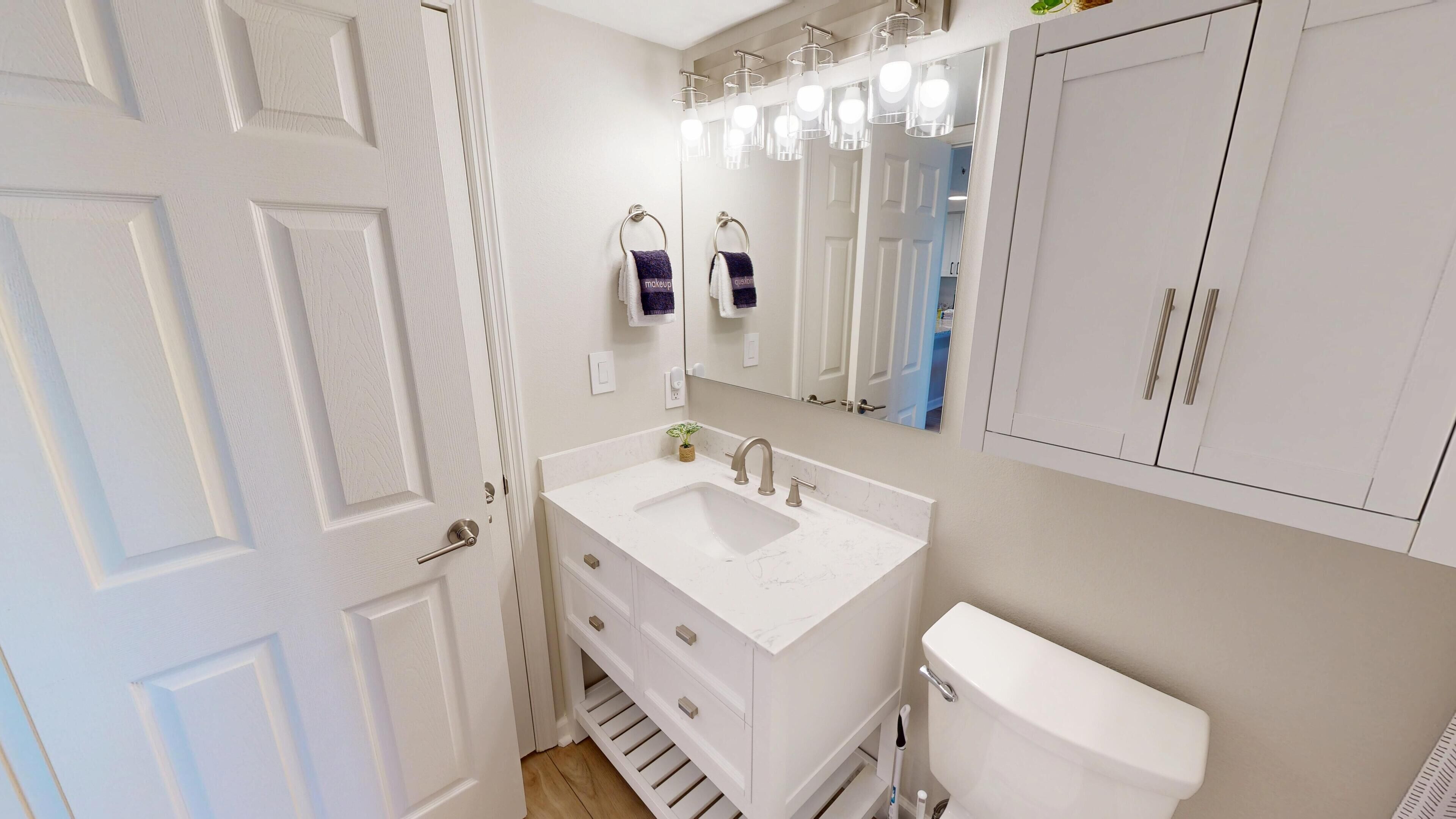Une salle de bain avec un lavabo blanc, un miroir et des toilettes. Deux serviettes sont accrochées au mur.