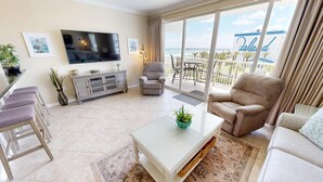 A modern living room with a flat-screen TV, comfortable seating, a balcony with a view of the sea, and a sign reading "The Island". - Beautiful DW Gulfside 403 (Fort Walton Beach)