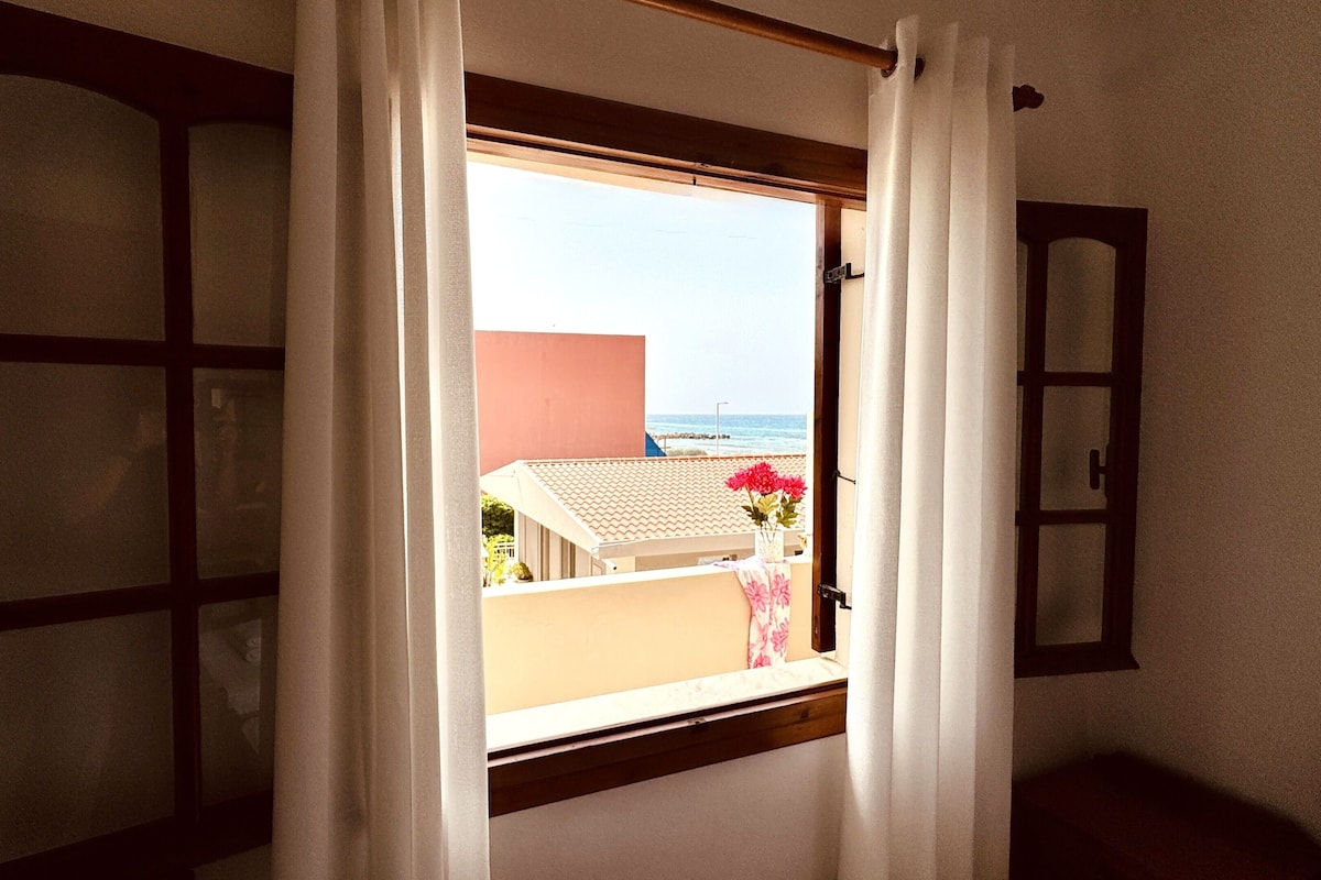 Une pièce avec une fenêtre donnant sur une plage, une porte et un miroir au mur.