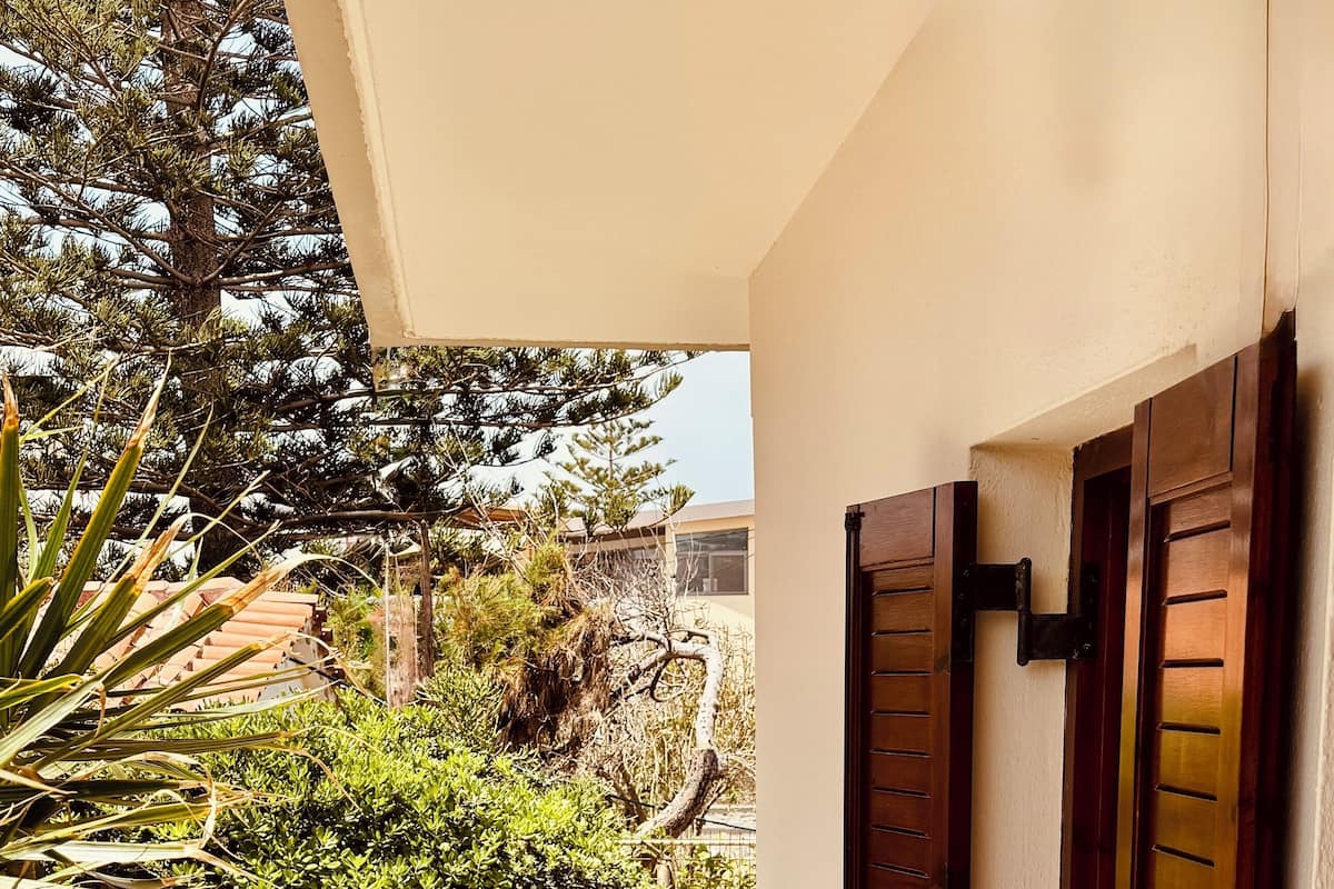Un balcon avec une table et des chaises, une porte en bois et de la verdure tout autour.