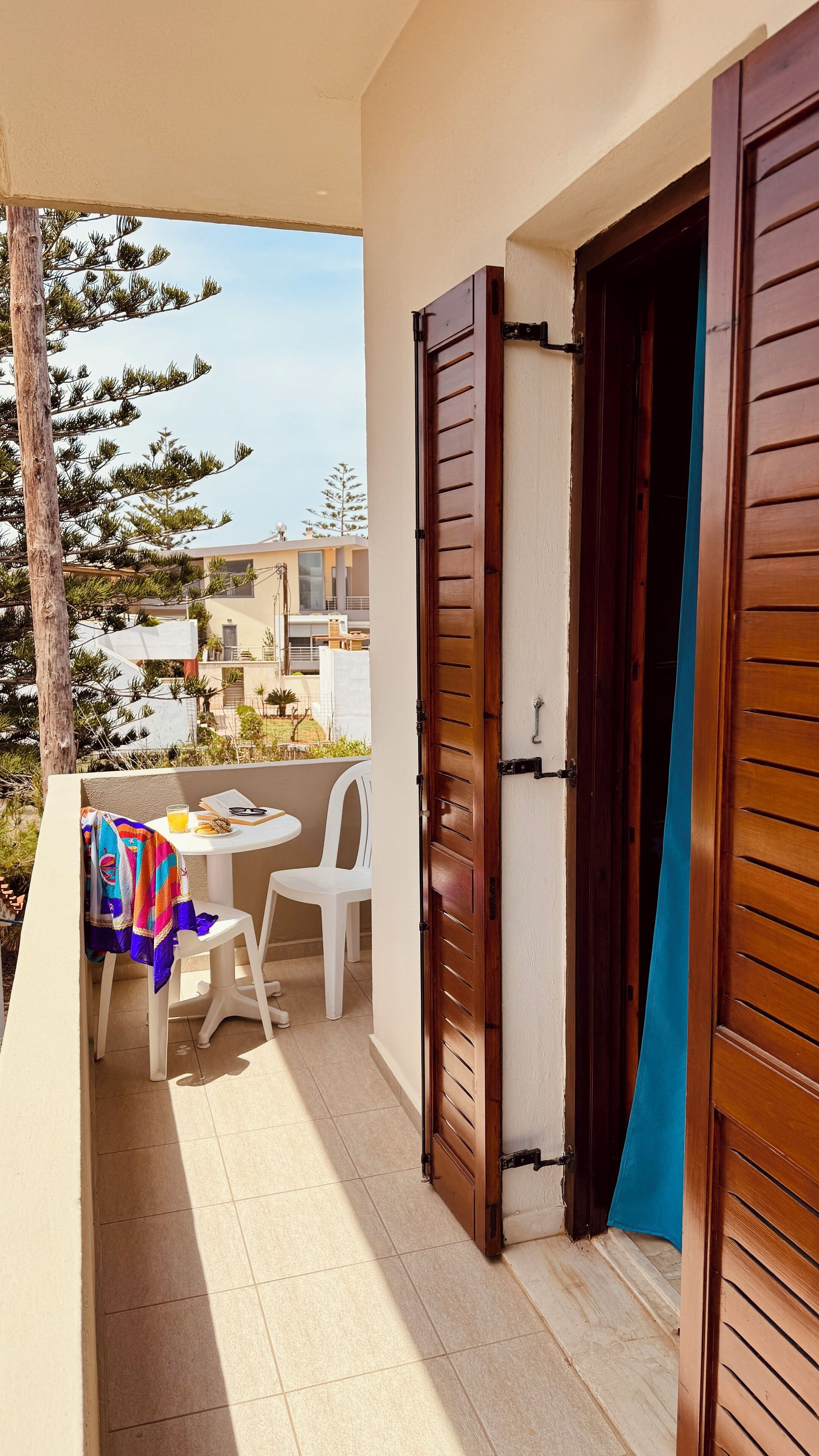 Un balcon avec une table, des chaises et une porte en bois entrouverte.
