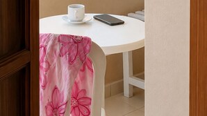 Parveke, jolta avautuu näkymä merelle, valkoinen pöytä, jonka päällä on kuppi ja älypuhelin, sekä vaaleanpunainen, kukkakuviollinen tuoli.
