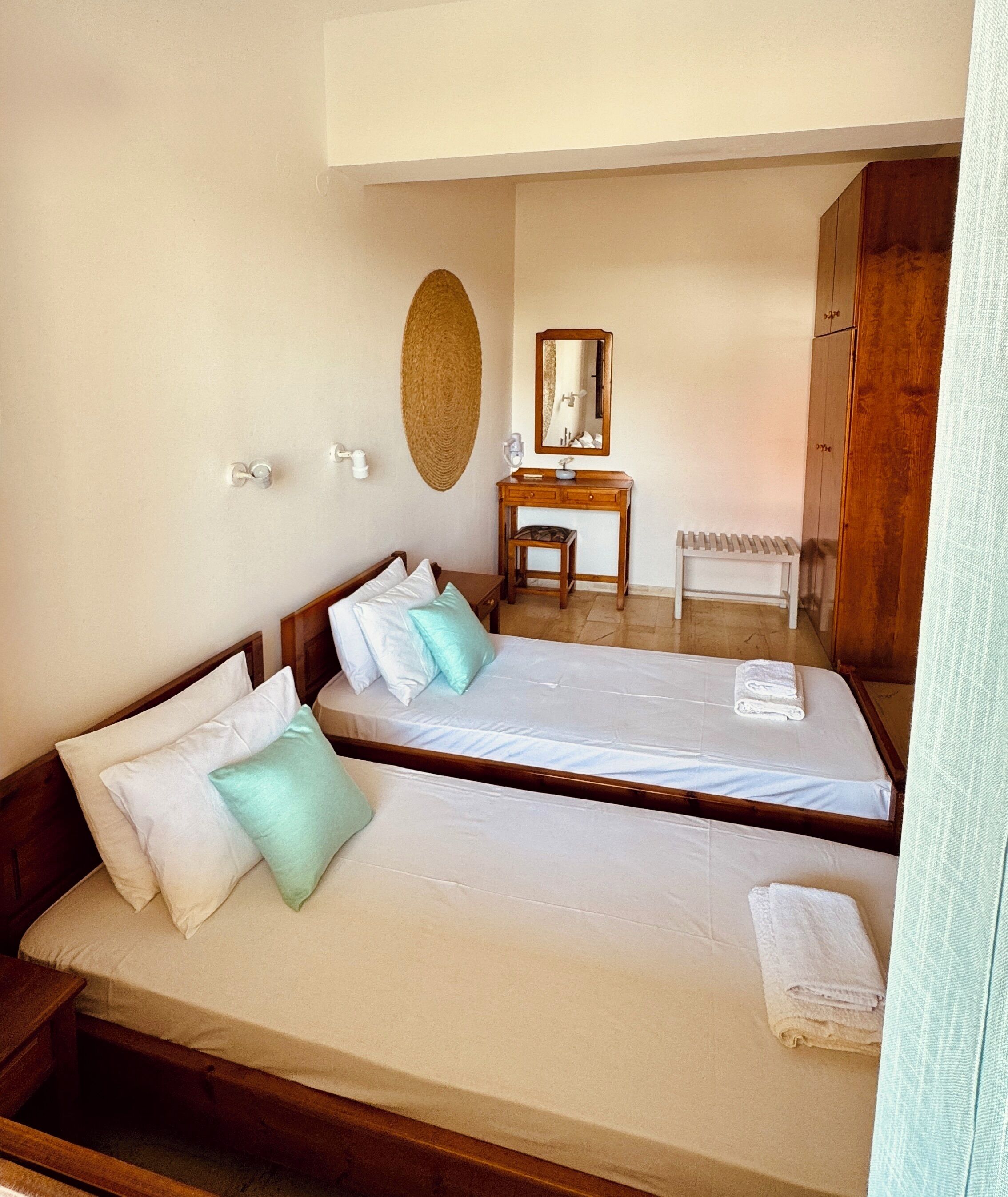 A hotel room with two beds, a wooden dresser, a small bench, and a mirror on the wall.
