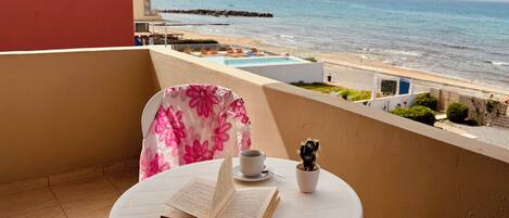 A balcony with a table, a chair, a book, a cup, and a cactus.