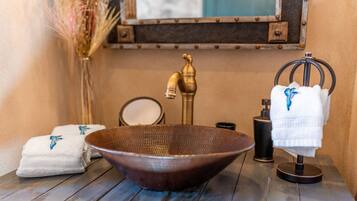 A bathroom with a wooden bowl sink, a brass faucet, a mirror, a towel rack, and a decorative vase.