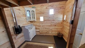 A wooden cabin interior with a built-in stove, a white cabinet, and a small rug. - Bright and Cozy Tiny Pine House (Erin)