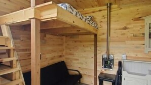 A wooden cabin interior with a bunk bed, a small table with a heater, and a black sofa. - Bright and Cozy Tiny Pine House (Erin)