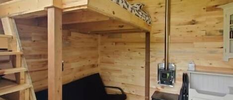 A wooden cabin interior with a bunk bed, a small table with a heater, and a black sofa.