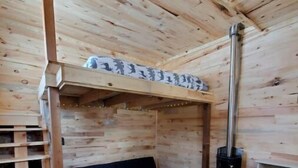A wooden cabin interior with a bunk bed, a black sofa, a fireplace, and a wooden ladder. - Bright and Cozy Tiny Pine House (Erin)