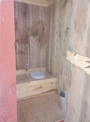 A wooden cabin with a single wooden bench and a white toilet.