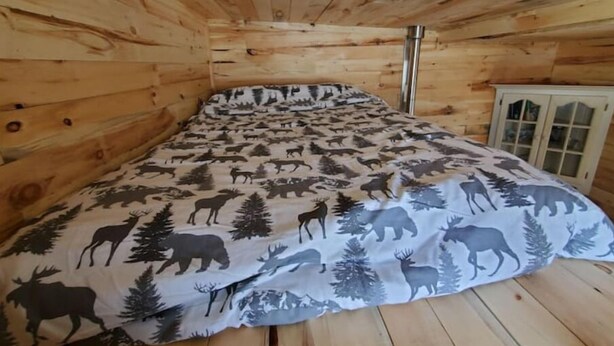 A room with wooden walls and a bed with a nature-themed duvet. - Bright and Cozy Tiny Pine House (Erin)