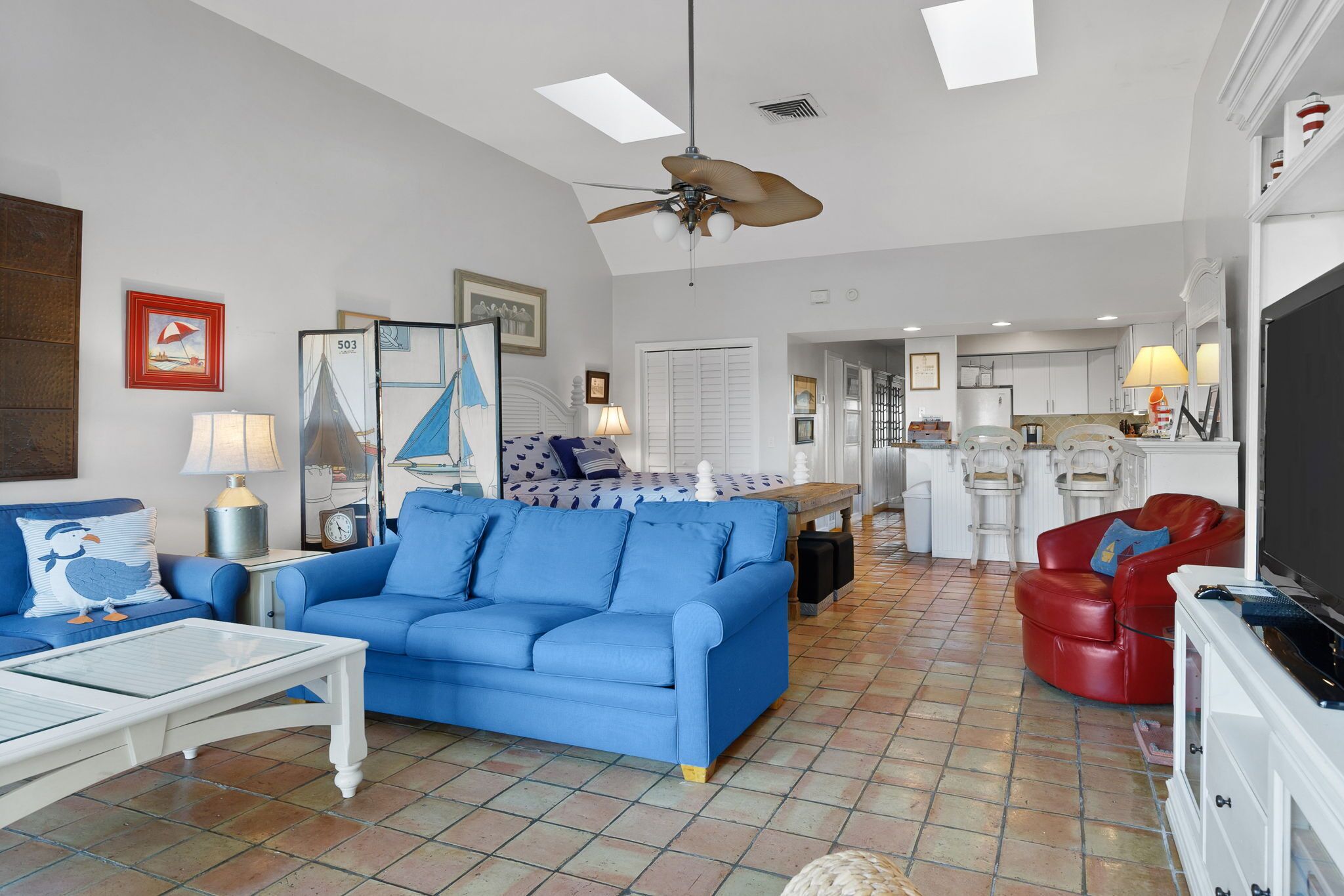 A living room with a blue sofa, a red armchair, a white coffee table, and a ceiling fan.